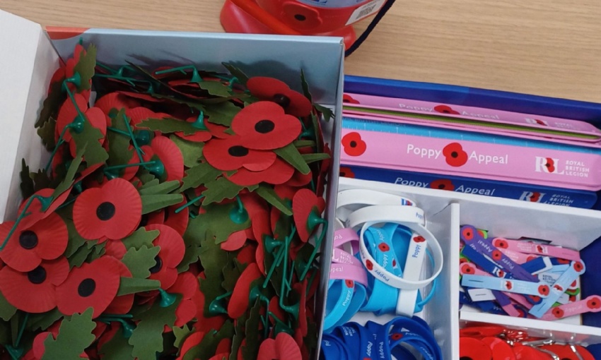 Image shows the collection tin and box of poppies, wristbands, bracelets and other items available to support the Royal British Legion